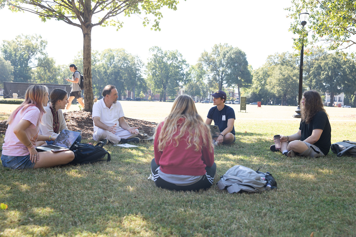 Students sit with their professor out on the Quad.