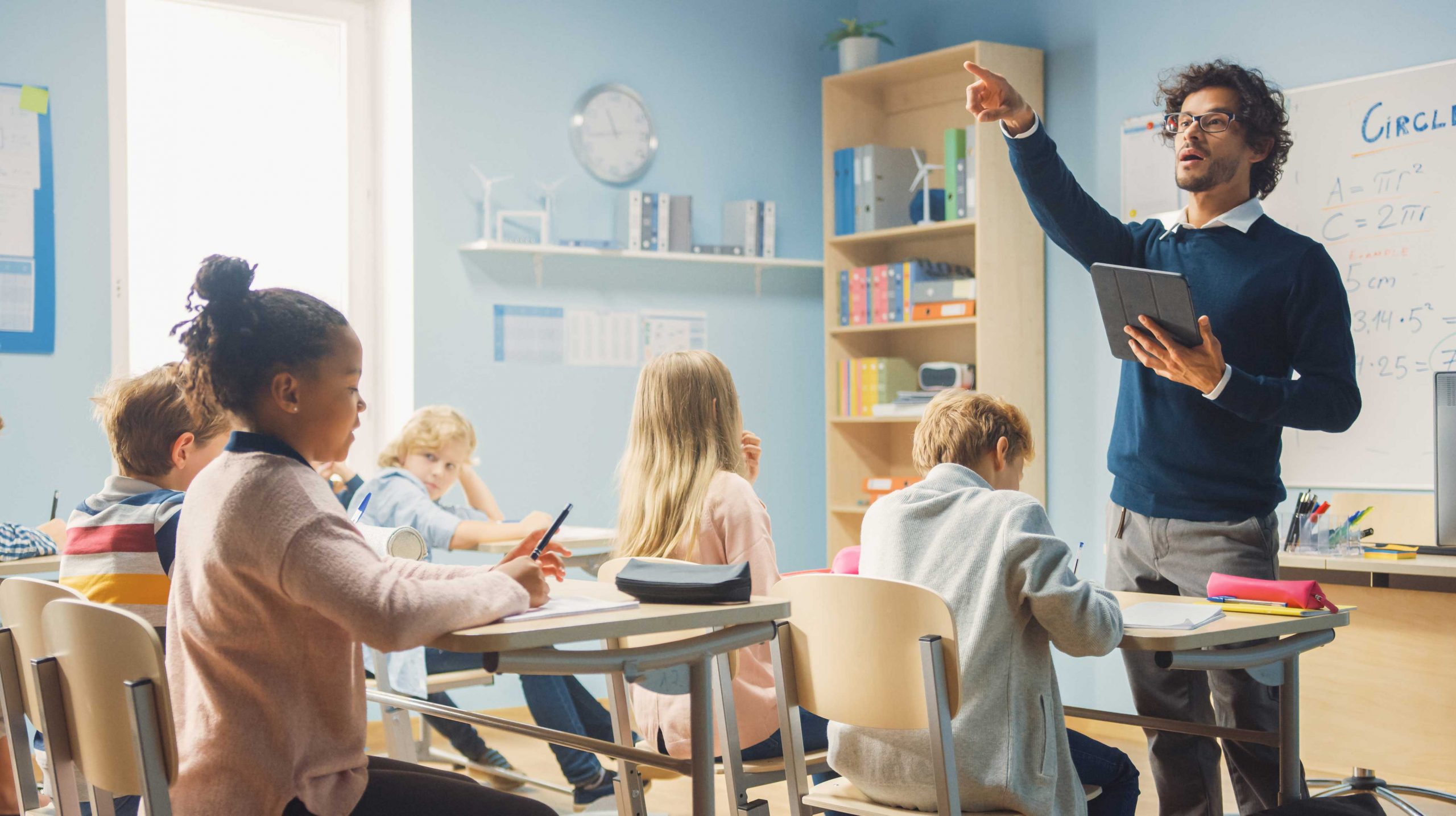 Enthusiastic Teacher Giving a Lesson in Elementary School to Class Full of of Diverse Children