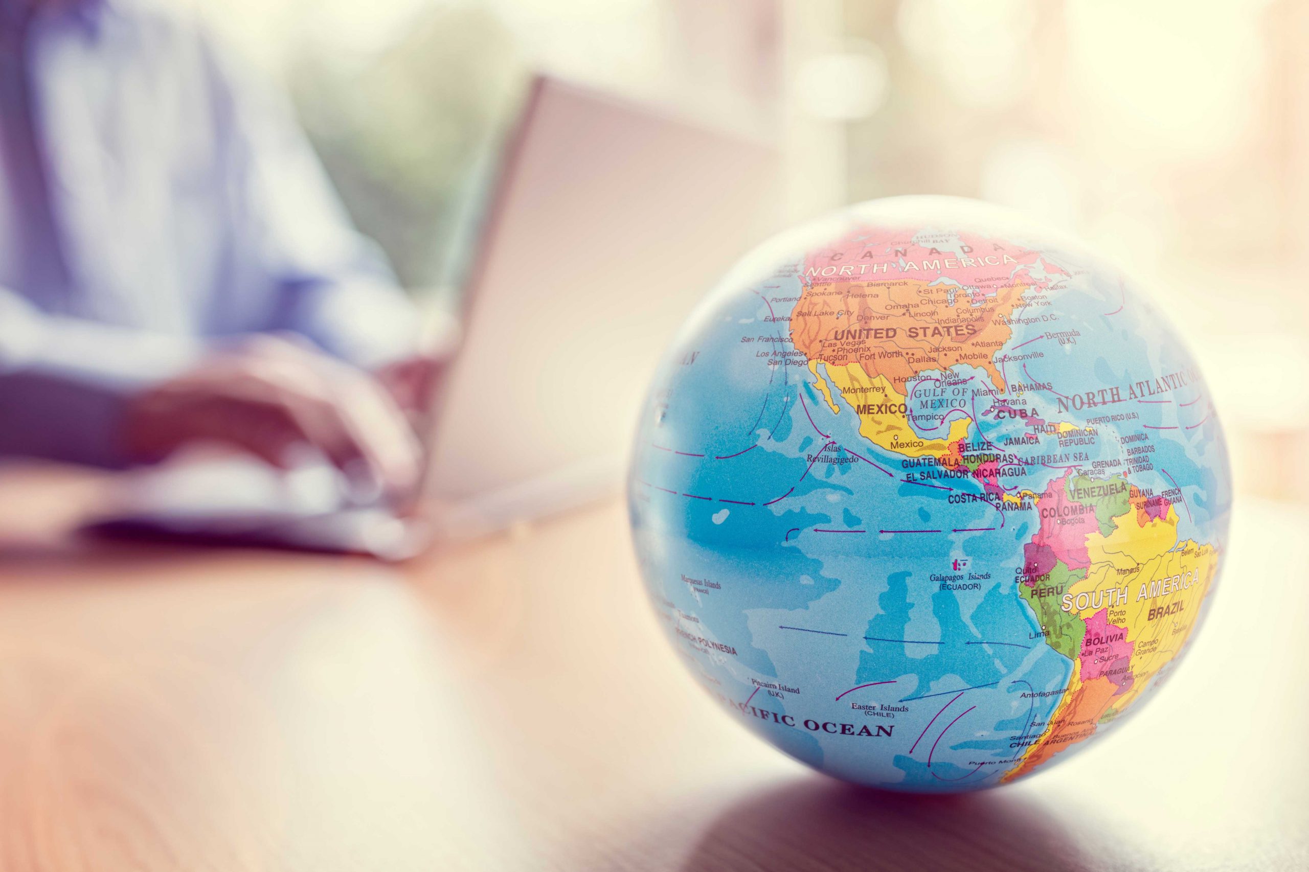 Globe sits in the foreground while someone works on a computer behind it.