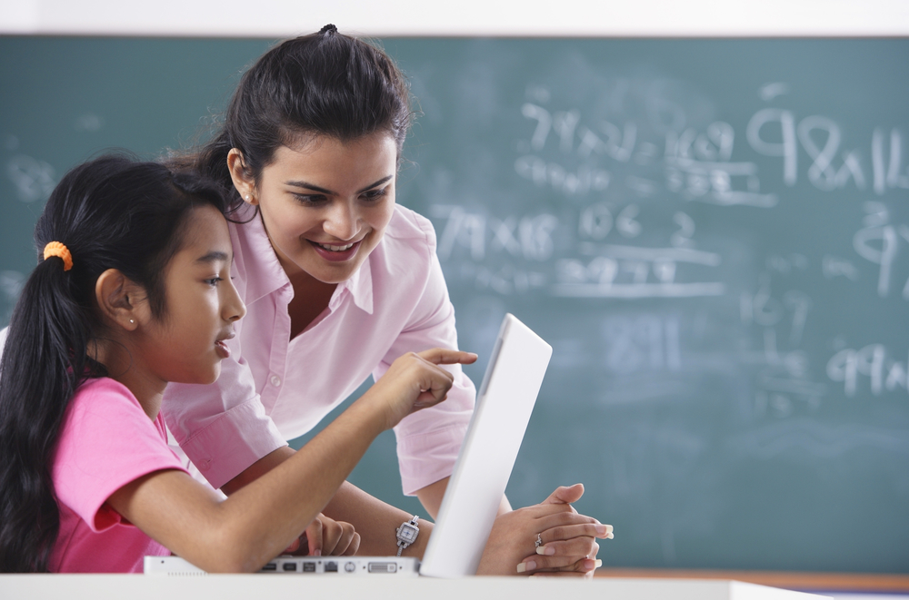 A teacher helps a student who is working on an assignment on a laptop.