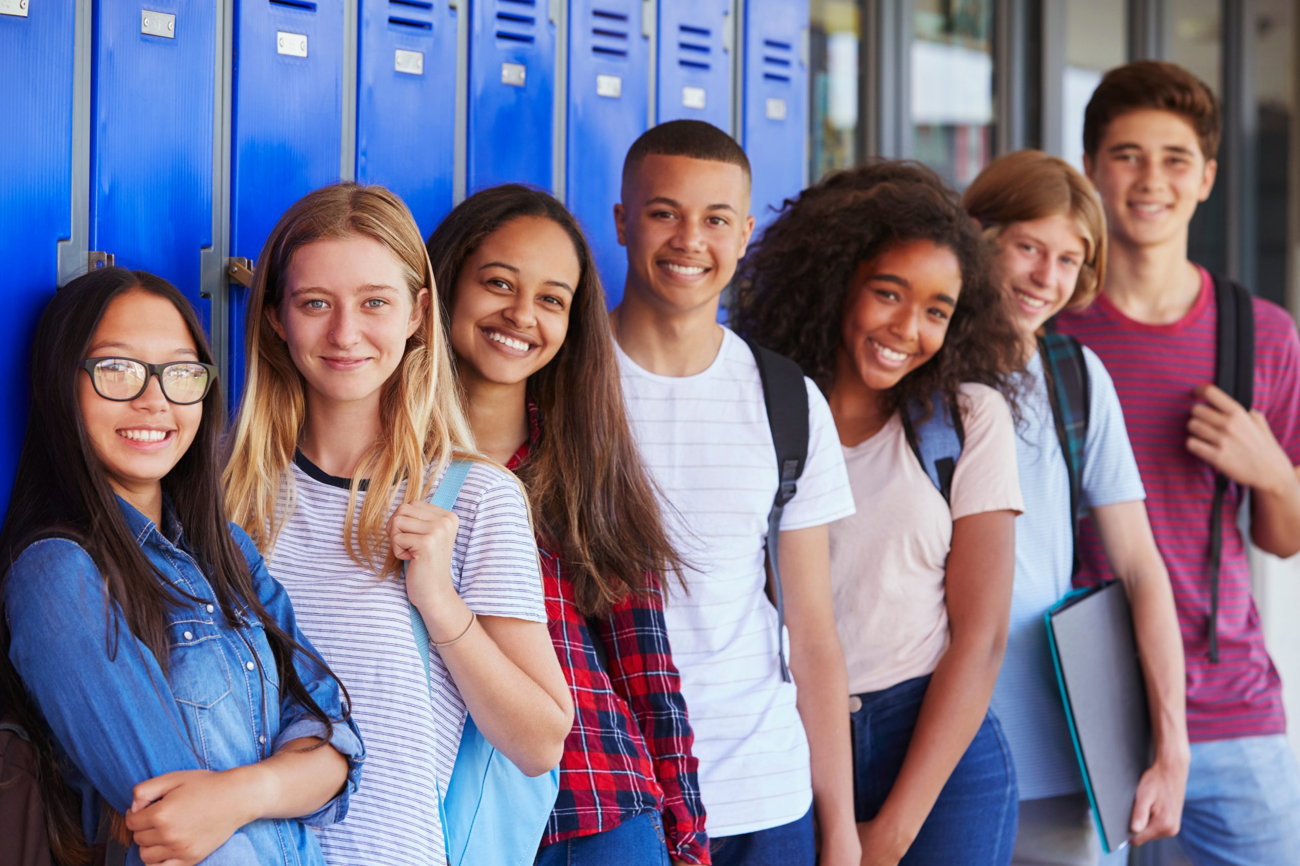 A group of teenagers stands in front of lockers.