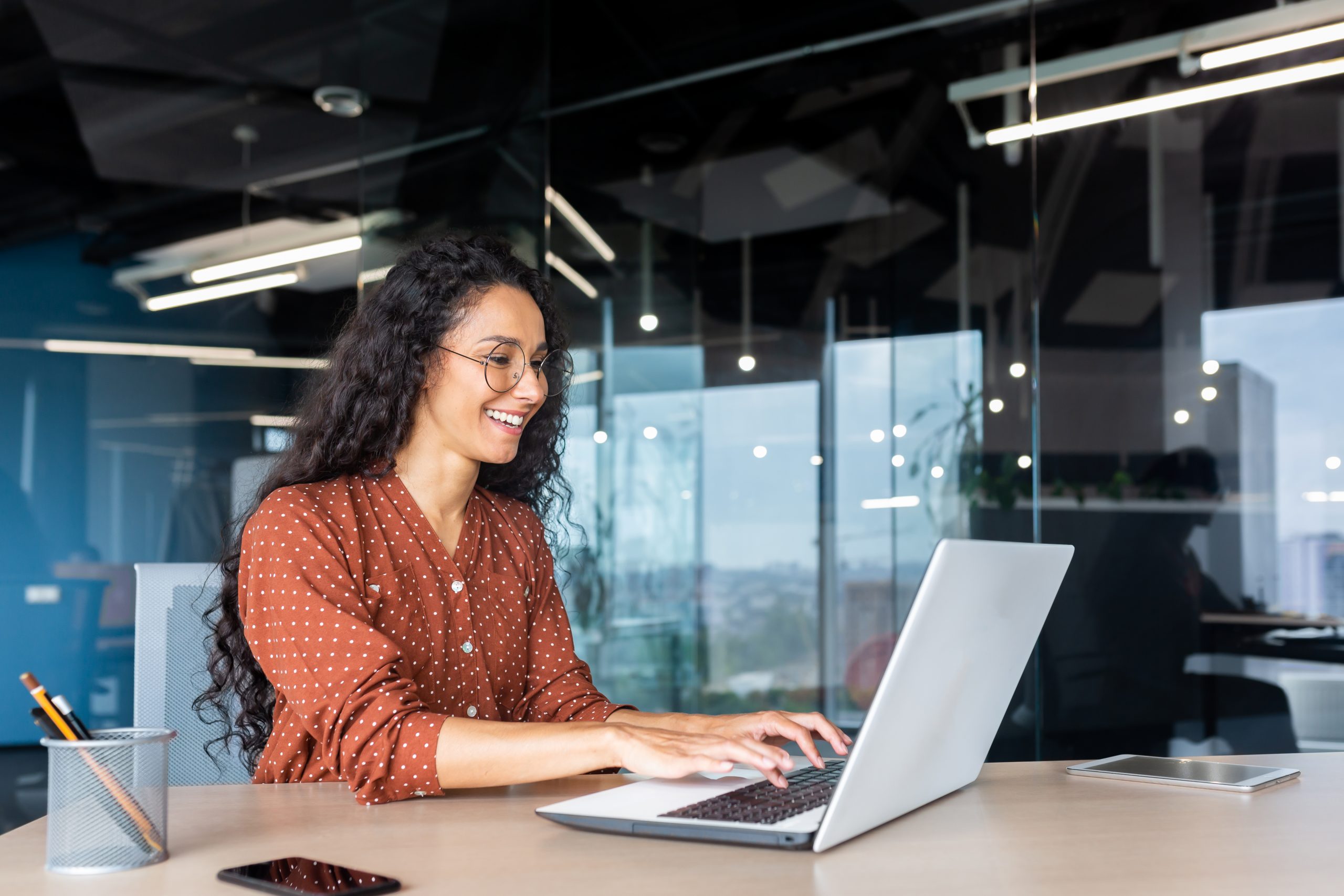Young woman in glasses smiles as she works on a laptop.