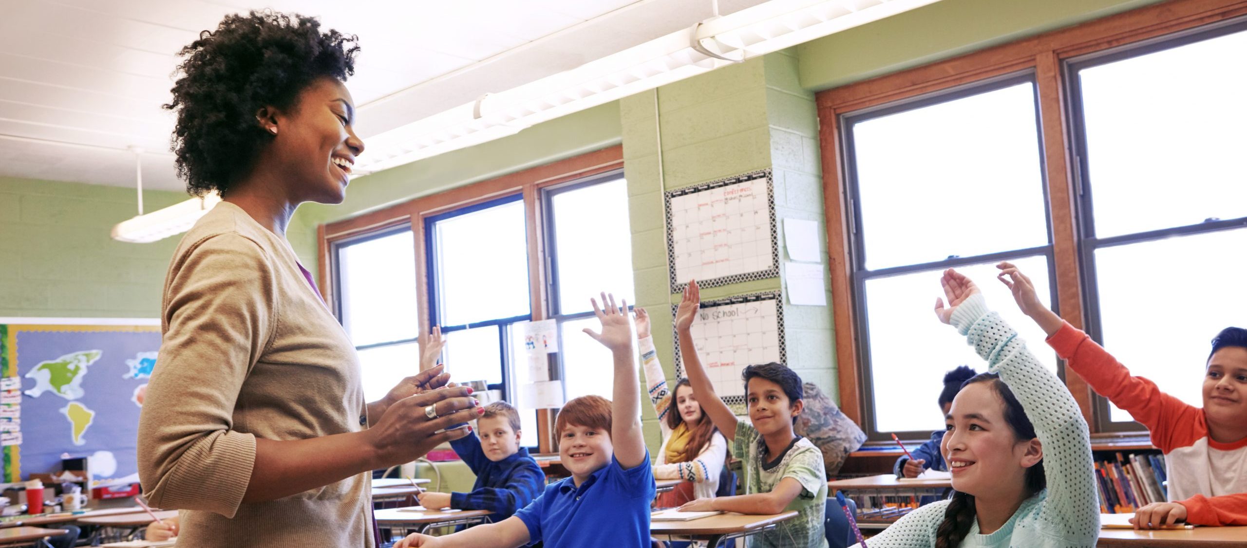 Children raise their hands to answer their teacher's question during class.