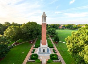 Denny Chimes sits on the Quad during a sunset, surrounded by green grass and lush trees.