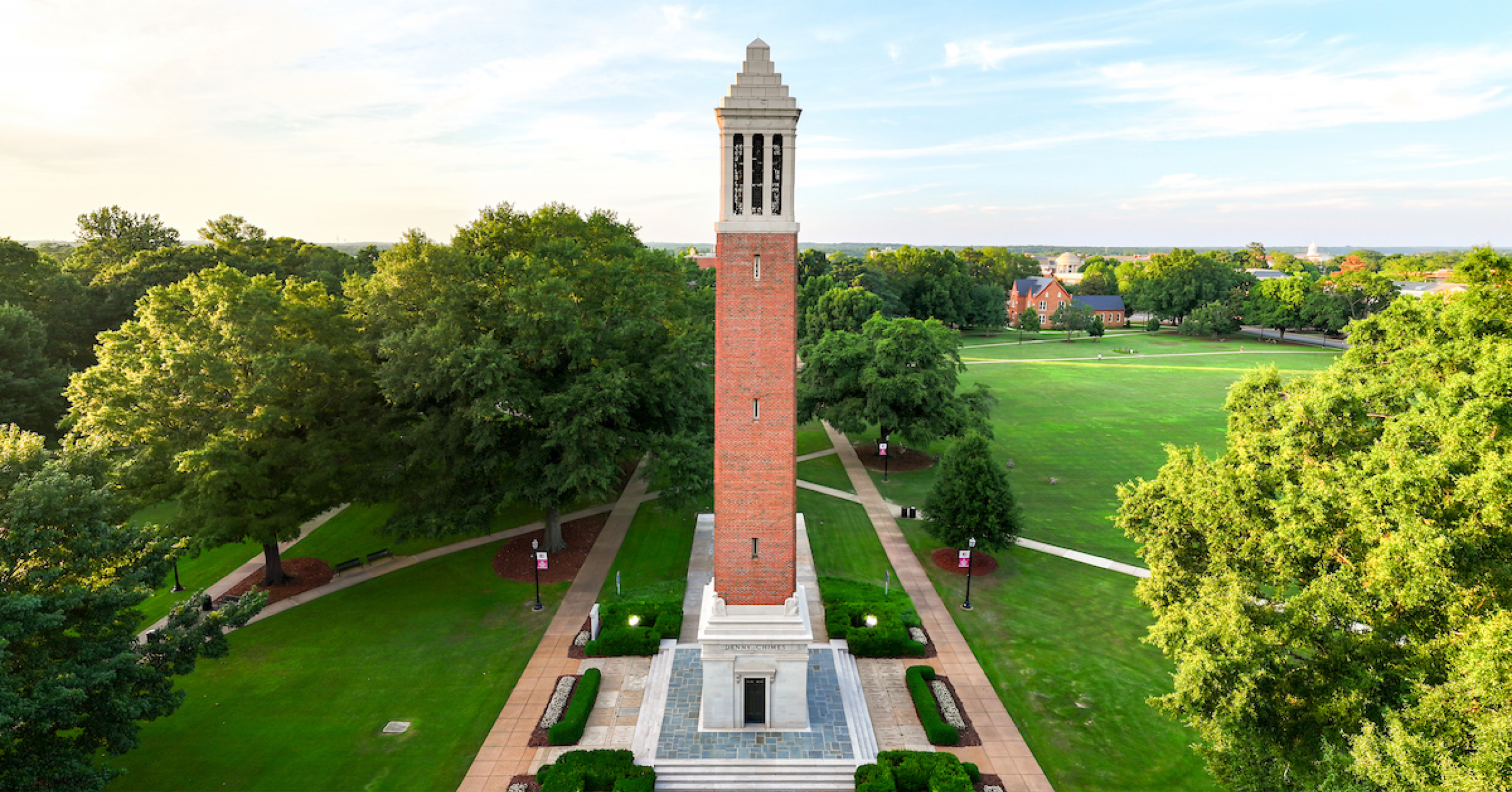 Denny Chimes sits on the Quad during a sunset, surrounded by green grass and lush trees.