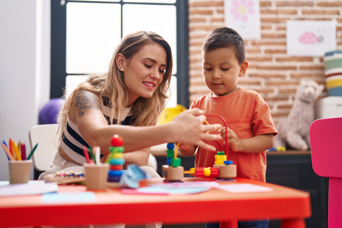 Young teacher with tattoo on her arm works with a child.